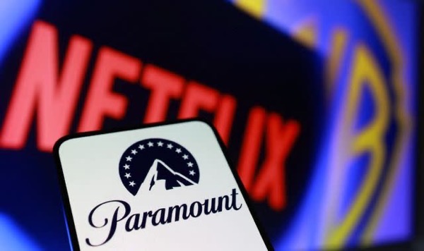 Smartphone screen showing the Paramount logo in sharp focus in the foreground, with a blurred Netflix logo and other colorful streaming imagery in the background, suggesting competition between streaming services.