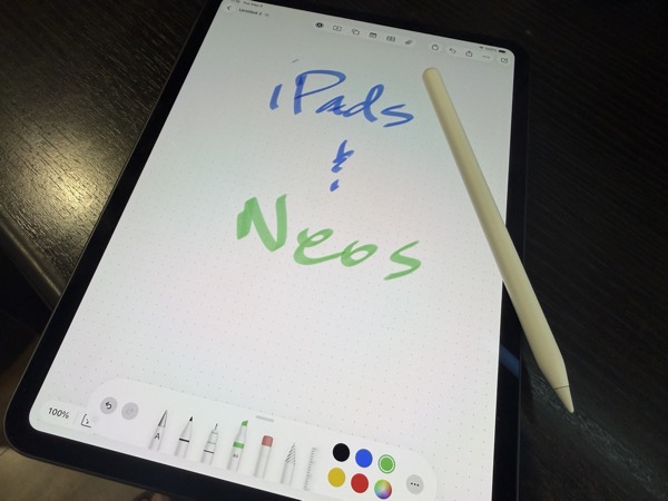 An iPad Pro with a scribbled message that says iPads and Neos. There is an Apple Pencil laying on the iPad