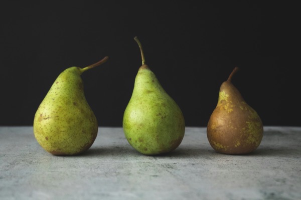 Three green pears on a table top in various degrees of ripening. Photo by Tijana drndarski 3zmVSZQIozA unsplash.