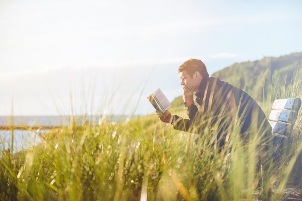 Ben white 1MHU3zpTvro unsplash. A man sitting by a lake or river, reading a book.